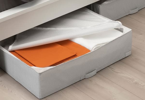 A STUK storage box is unzipped halfway through, showing folded bed linen inside of it.