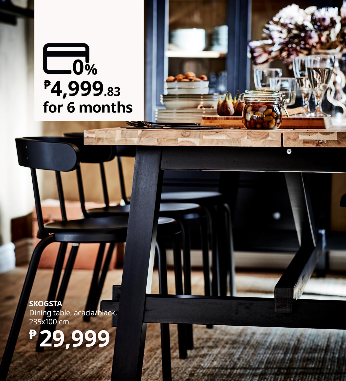 A stylish dining table in acacia wood, surrounded by black chairs, featuring a variety of dishes and elegant glassware on it.
