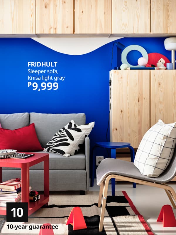 A stylish living room featuring a gray sleeper sofa, red coffee table, and blue wall, promoting FRIDHULT furniture for ₱9,999.