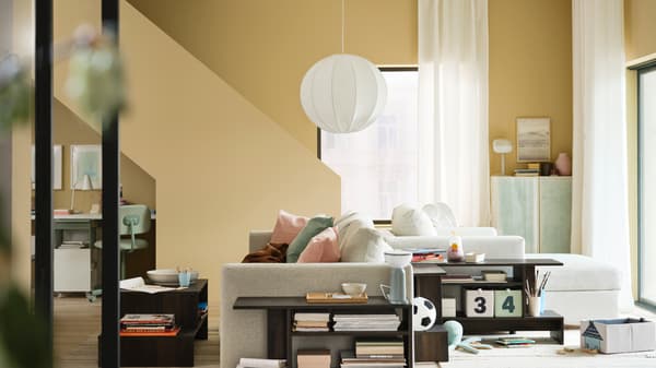 A stylish living room has yellow walls and a beige VIMLE 2-seat sofa back-to-back with a beige VIMLE chaise longue.