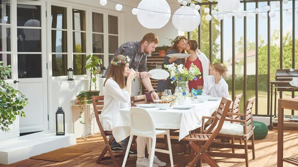 A sunlit roofed terrace with people around a table decorated with flowers, hanging lanterns and a small Swedish flag.