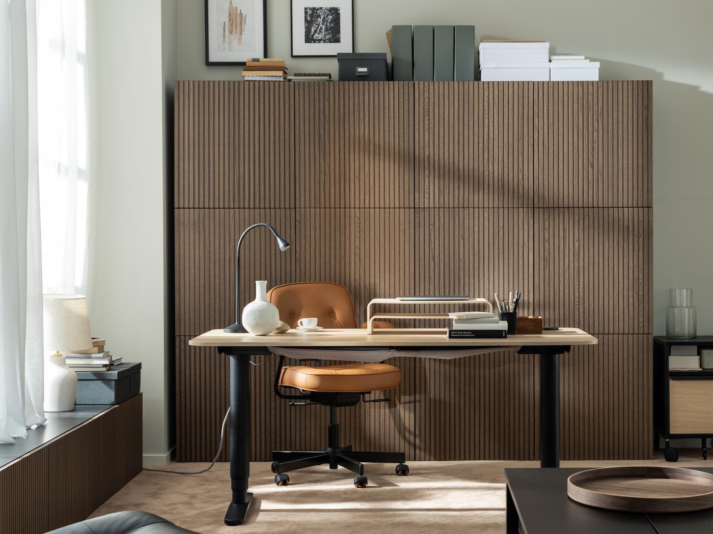 A sunlit workspace formed by a BEKANT sit-stand desk, an ALEFJÄLL office chair and a wall of wood-front BESTÅ cabinets.