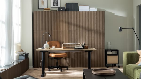 A sunlit workspace formed by a BEKANT sit-stand desk, an ALEFJÄLL office chair and a wall of wood-front BESTÅ cabinets.