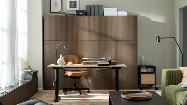 A sunlit workspace formed by a BEKANT sit-stand desk and an ALEFJÄLL office chair in front of a wall of wood-front cabinets.