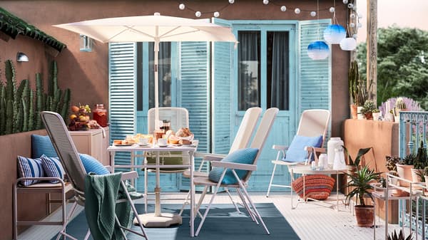 A sunny patio with terracotta walls, blue doors, a white table with parasol, white outdoor chairs and blue cushions.