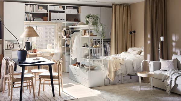 A sunny studio flat with white PLATSA storage combinations and bed frame, a black LISABO table and RÖNNINGE chairs.