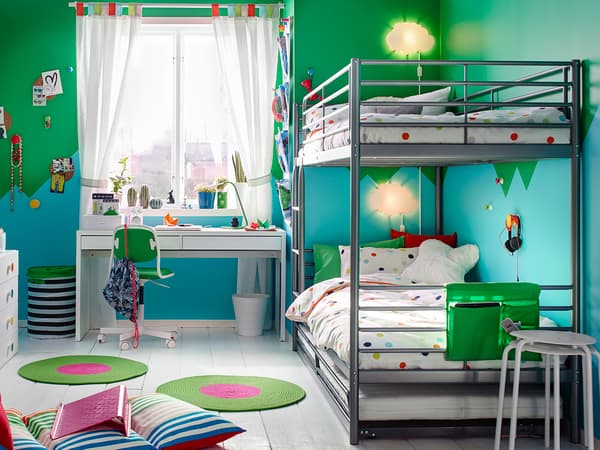 A SVÄRTA bunk bed frames with printed duvets and a white desk in a children's bedroom.