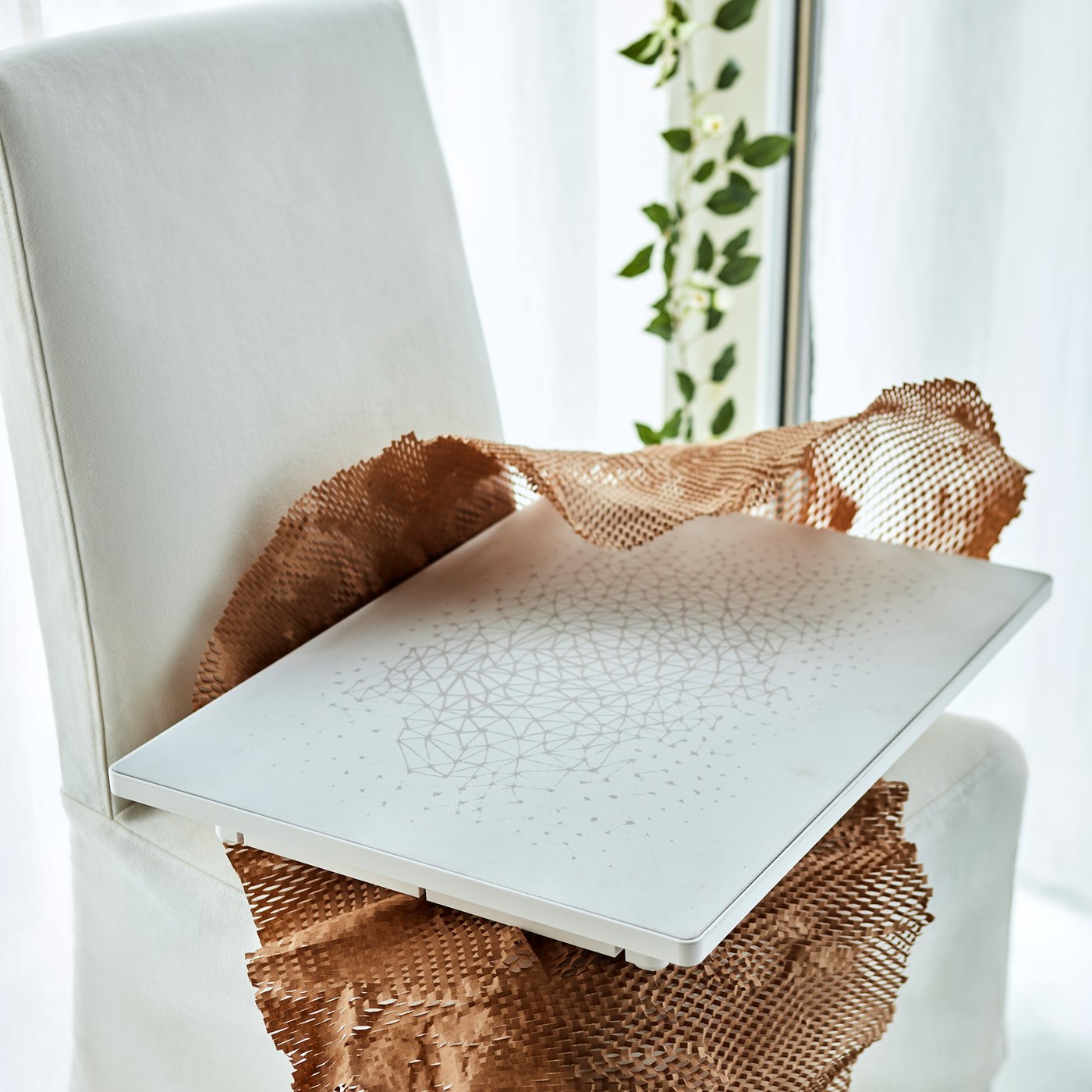 A SYMFONISK picture frame with a WiFi speaker with a graphic print lying on some netting on a textile chair.