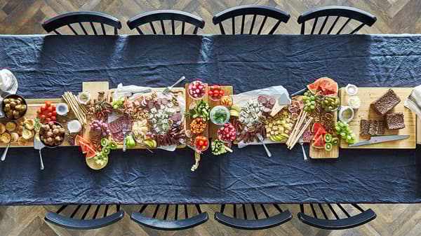 A table covered in a blue table cloth with a row of wooden chopping boards going down the middle full of cold foods.