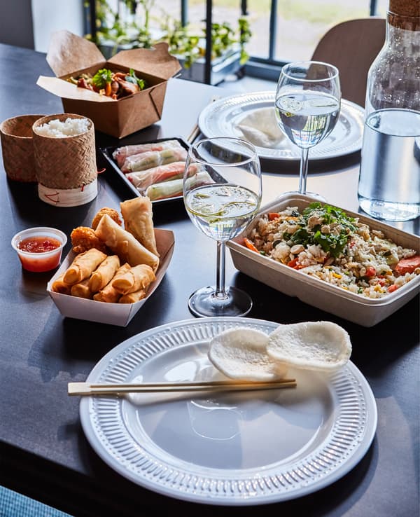 A table is set with wine glasses, tableware, and Asian takeout containers.