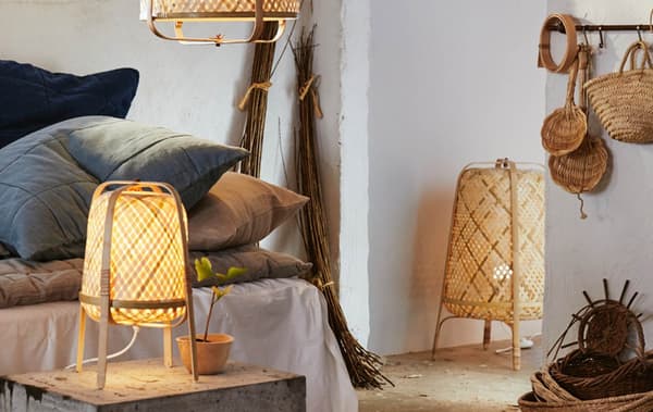 A table lamp, pendant lamp and floor lamp with weaved shades in a room with stone white walls and a seat with large cushions.