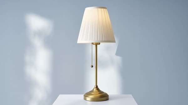 A table lamp with a white shade and gold base sitting on a nightstand.