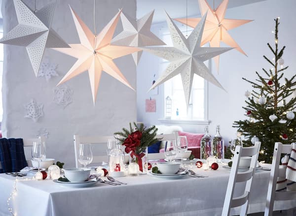 A table set for dining with festive holiday decoration, white chairs, and paper star lanterns hanging above.