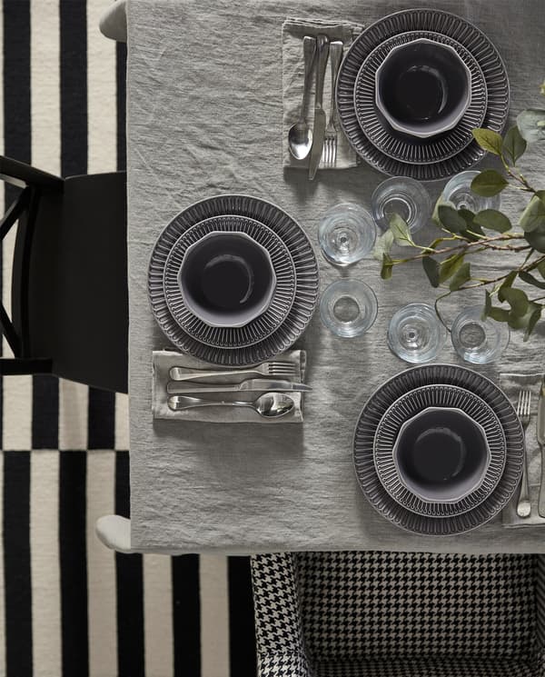 A table set with a grey tablecloth, grey linen napkins, plates and bowls in earthenware grey and cutlery in stainless steel.