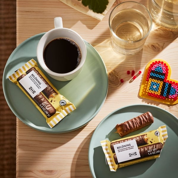 A table setting with a cup of black coffee, a glass of water and chocolate bars on greenish plates.