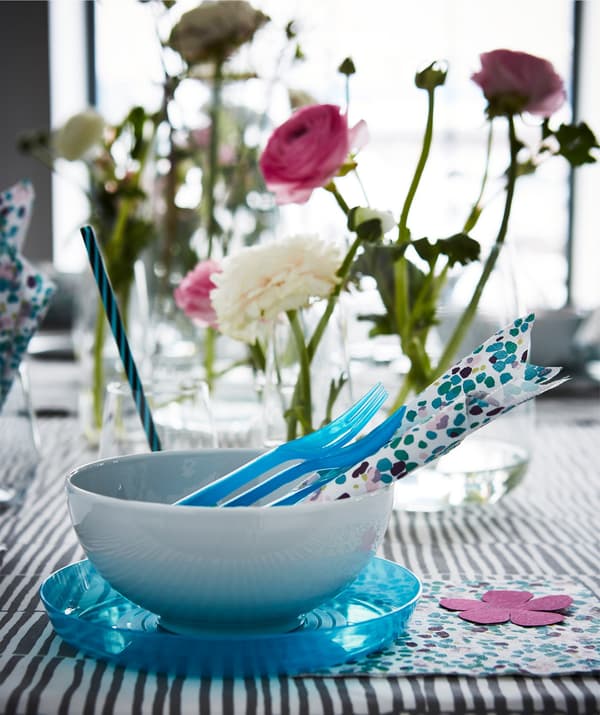 A table setting with blue and white dinnerware with multicoloured paper napkins and flowers.