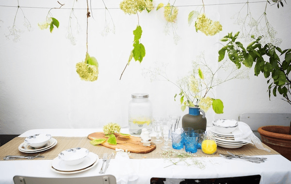 A table setting with patterned crockery, glasses and a vase of flowers, with flowers hanging above.