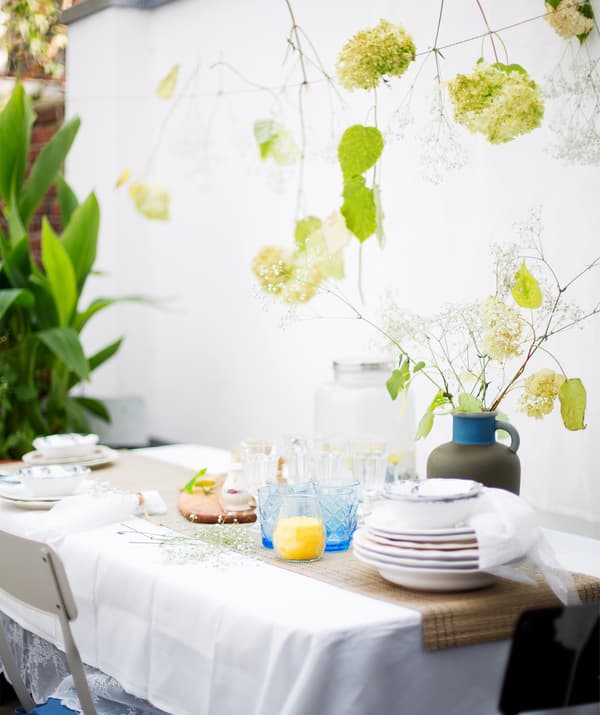A table setting with stacked plates, glasses and a vase of flowers, with flowers hanging on string above.