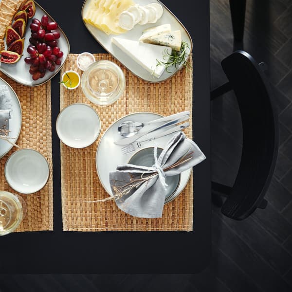 A table that’s set with place mats made from water hyacinth, grey dinnerware and two serving plates with cheese and grapes.
