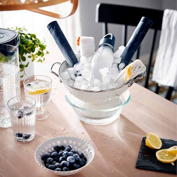 A table with different cooling systems, such as a jug and glasses of icy water and a colander filled with ice that has been placed within a dish.