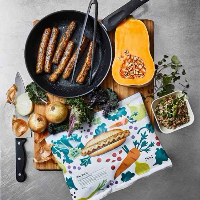 A table with different products to make a meal: a frying pan with vegan sausages, a pumpkin cut in half, some onions, etc. 