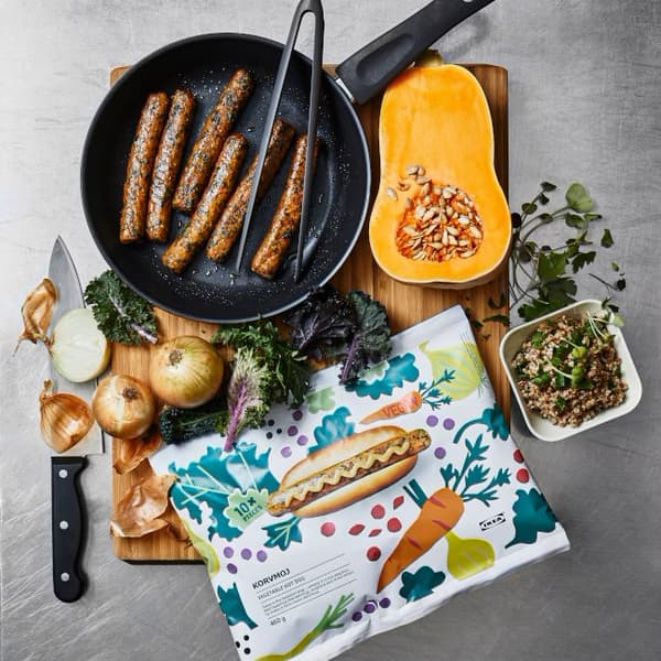 A table with different products to make a meal: a frying pan with vegan sausages, a pumpkin cut in half, some onions, etc. 