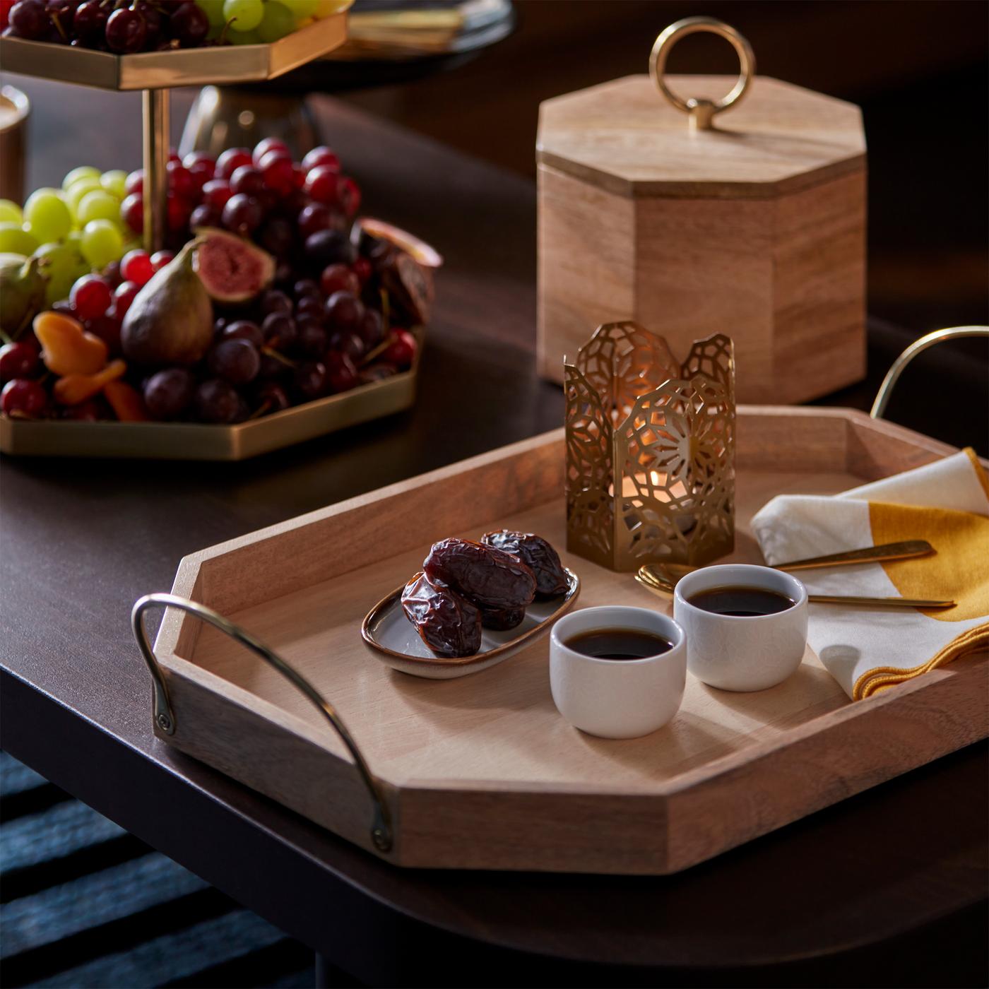 A table with GOKVÄLLÅ serving trays and a box with lid on it. There are kava cups, a tealight holder and fruit on the trays.