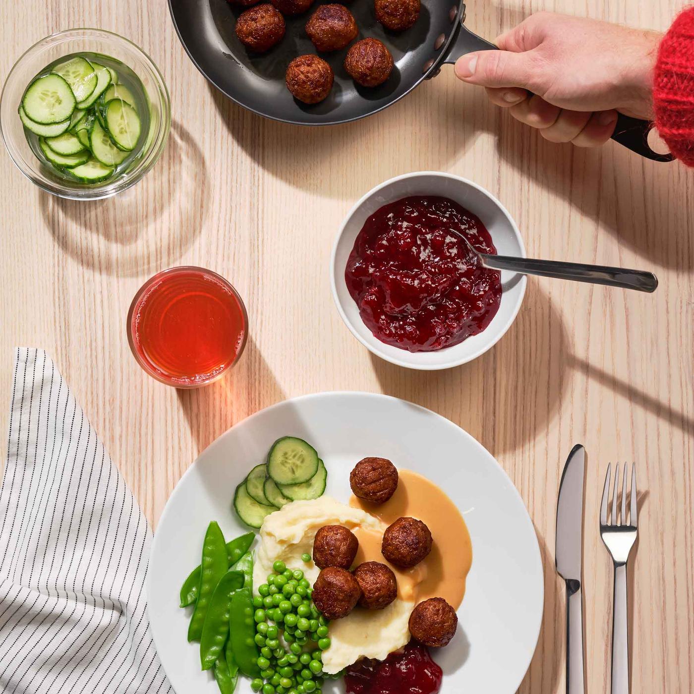 A table with meatballs in a pan and a dinner plate featuring meatballs, mashed potatoes, and peas.