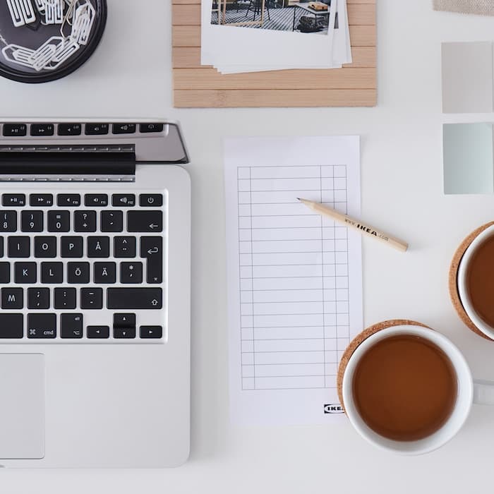 A table with two cups of tea, a computer, a notebook and several square color samples