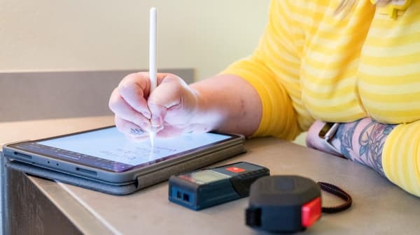 A tablet on which someone is drawing a kitchen plan with a stylus. Next to it are a measuring tape and laser measuring device. 