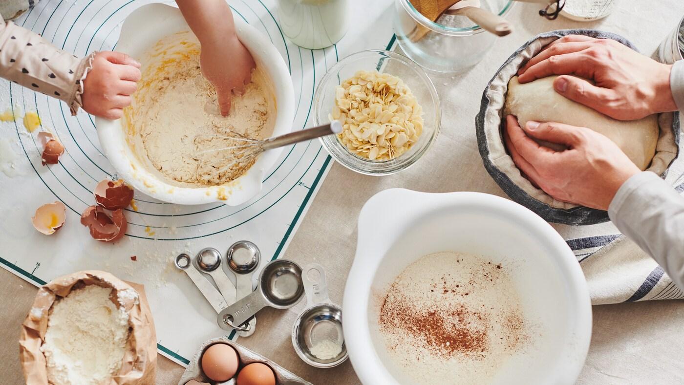 A tabletop mid-baking session – eggs, flour and utensils. Hands work doughs in white VISPAD mixing bowls and in a banneton.