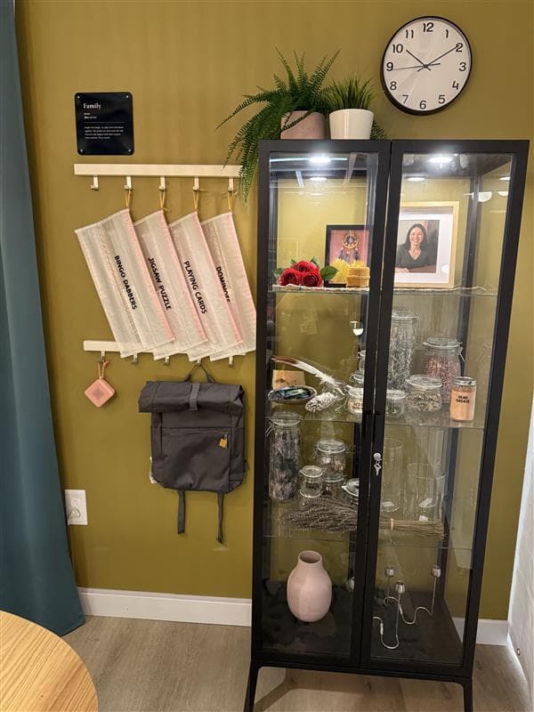 A tall black glass cabinet sits against a wall filled with home decor accessories.