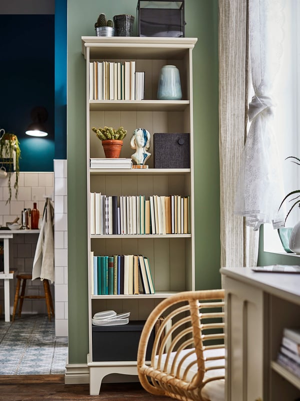 A tall bookcase with books against a green wall.