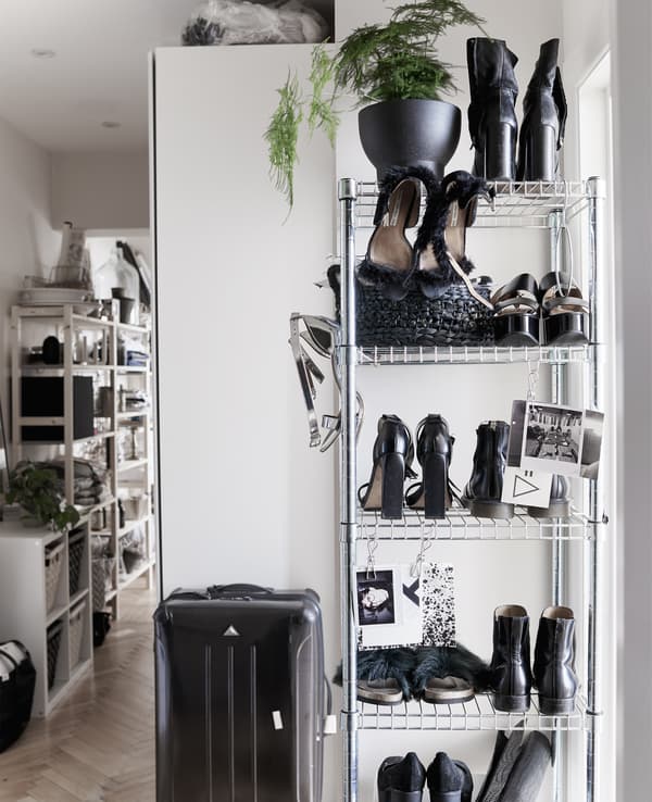 A tall open-storage shelving unit filled with shoes and a black suitcase.