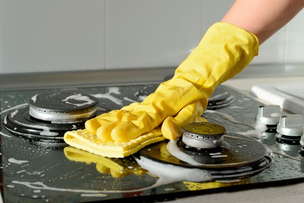 A Task Rabbit tasker wearing yellow rubber gloves whilst cleaning the hob with a sponge and cleaning products. 