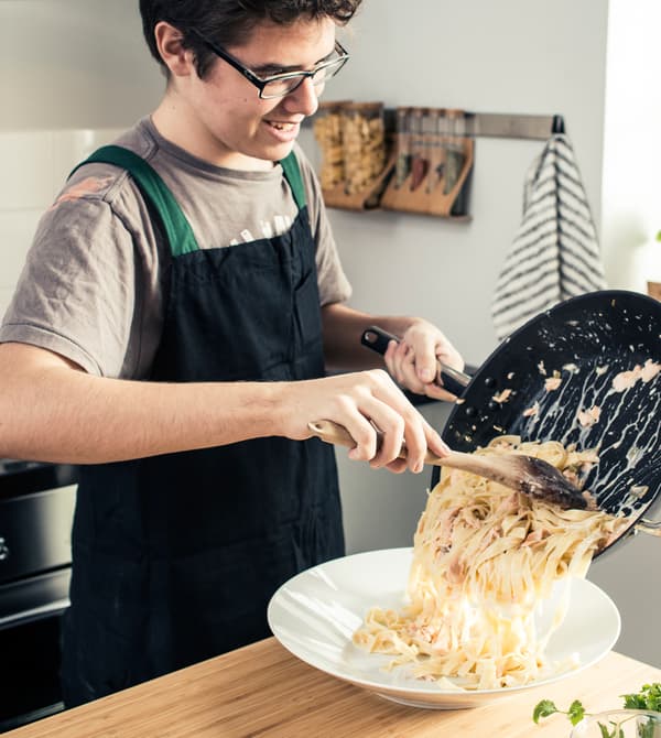 A teenage boy serving pasta into a bowl