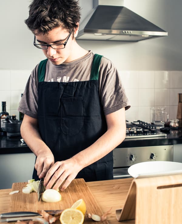 A teenage boy slicing an onion