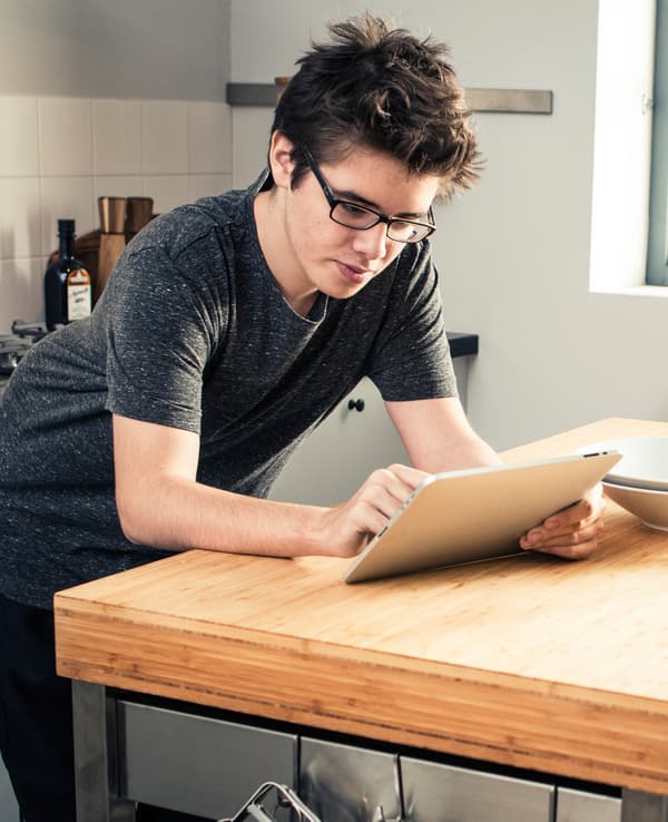 A teenage boy using a tablet in a kitchen