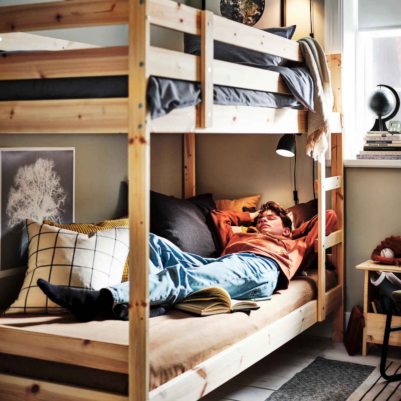 A teenager asleep on a pine MYDAL bunk bed with the top bunk dressed in a dark blue KOPPARBLAD duvet cover and pillowcase.