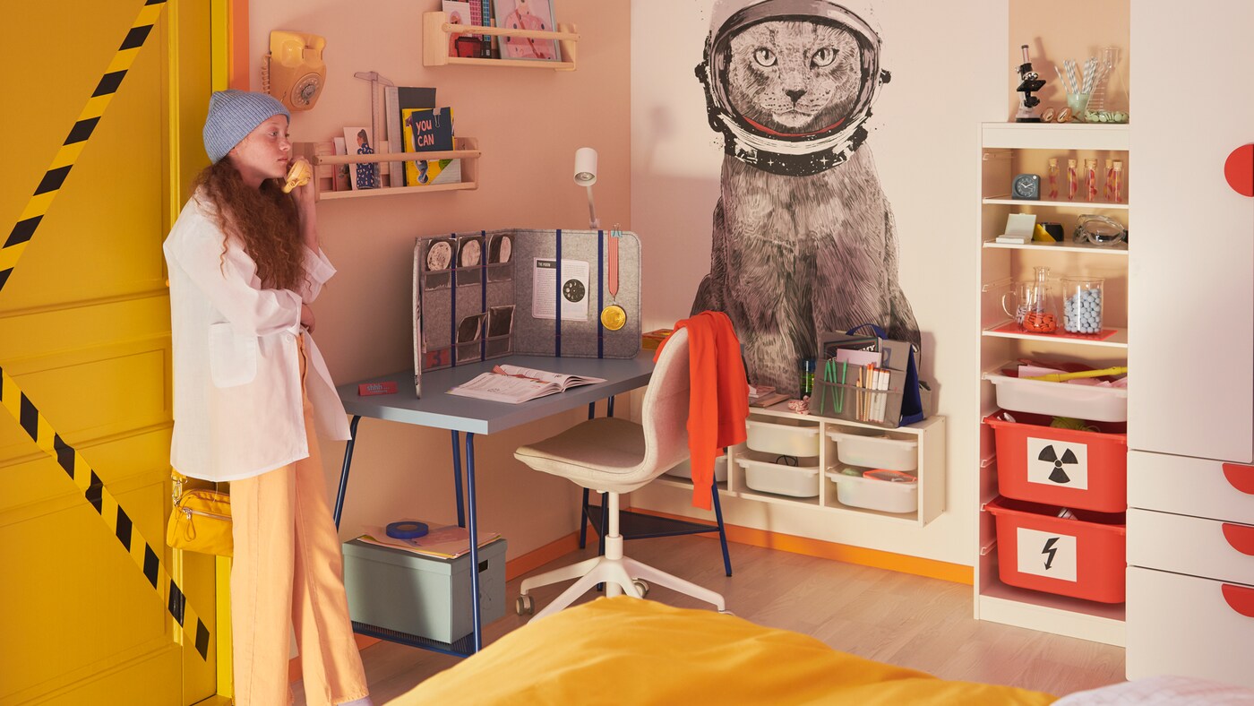 A teenager girl stands in her bedroom, with orange and white TROFAST boxes stacked neatly in her TROFAST frames.