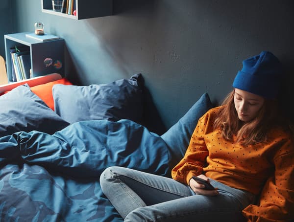 A teenager lounging on a bed on a mobile device.