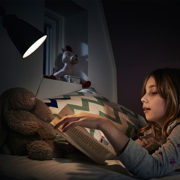 A teenager lying on her bed, reading beside a bed lamp with a RYET LED bulb.