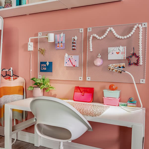 A teen's workspace shows a neatly organized desk with a plant, storage containers, and a work lamp on top. Two pegboards are placed side by side on the wall above the desk.