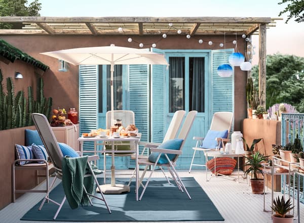  A terrace decorated in shades of blue with a patio table, folding chairs and colourful potted plants.