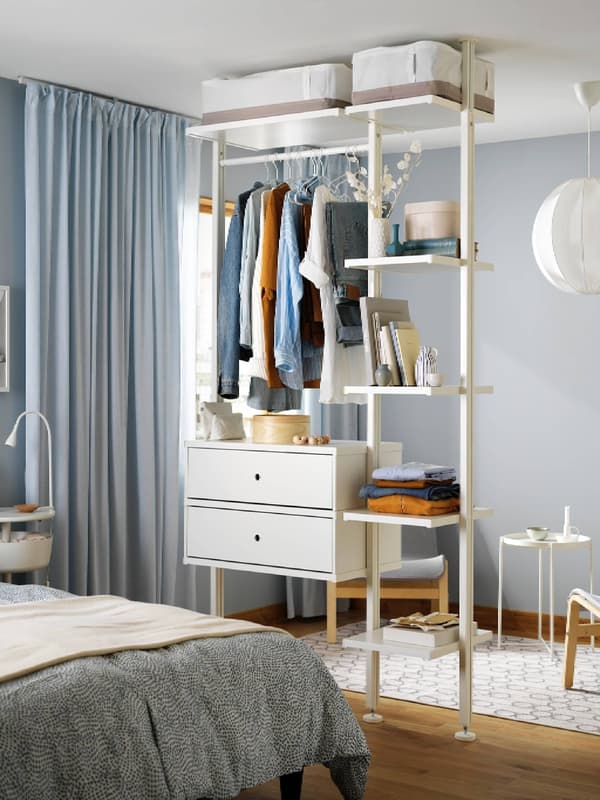 A textile sheath turns an IVAR shelving unit standing in a minimalistic, grey room, into a wardrobe, filled with clothing.