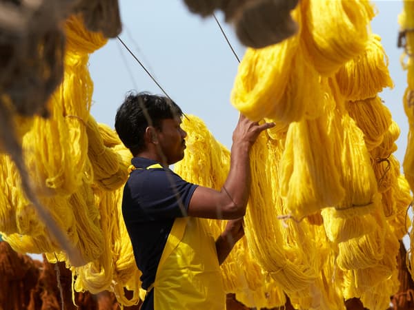 A textile worker in India hanging newly dyed, bright yellow cotton out to dry.