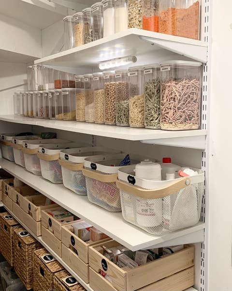 A tidy pantry with RISATORP baskets containing cleaning supplies, wooden KNAGGLIG crates with provisions, and BRANÄS baskets on the floor.