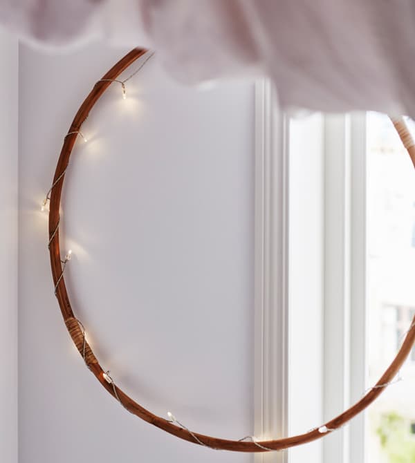 A timber hoop strung with fairy lights hangs from the wall, partially in front of a window.