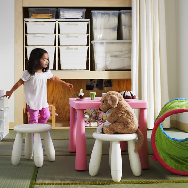 A toddler having a tea party with a soft toy, open storage in the background.