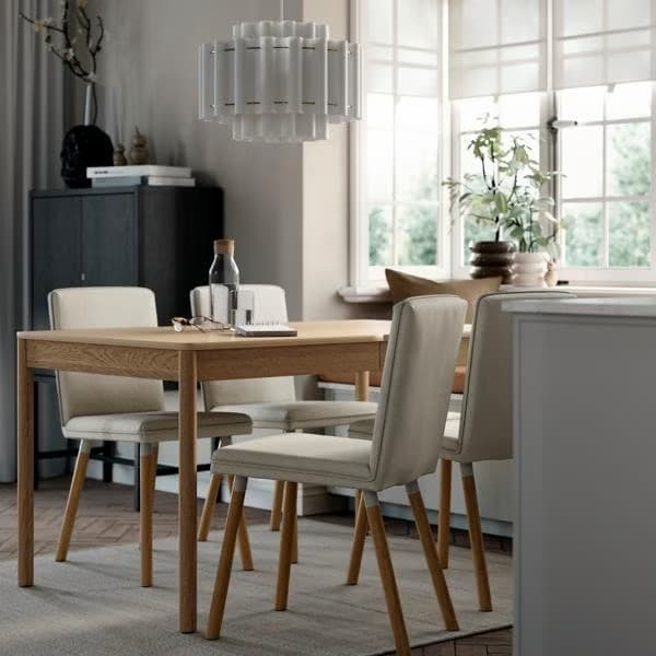 A TONSTAD extendable table in oak veneer set in a dining space with four grey chairs and natural light from large windows.
